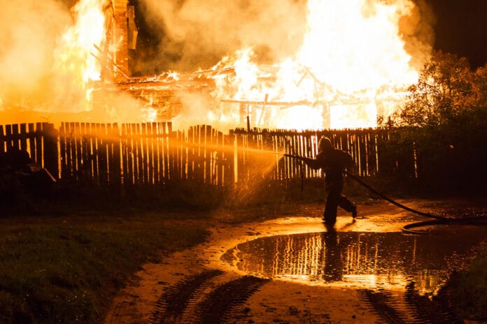Firefighter spraying water from hose on burning house at night