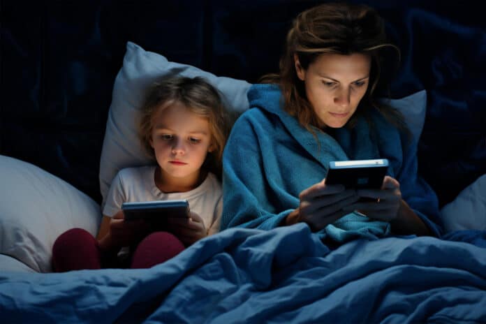 Mom and girl daughter lie on the bed looking at their phones before going to bed