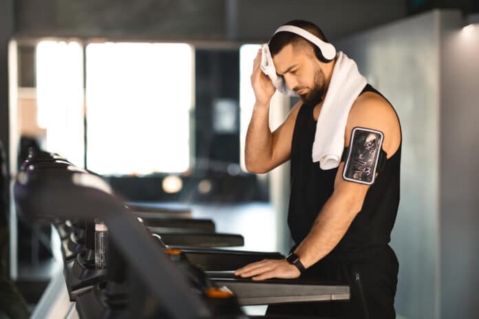 Determined young man wiping sweat after treadmill workout
