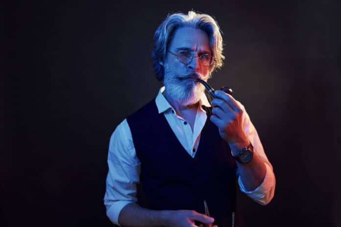 smoking Stylish modern senior man with gray hair and beard is indoors